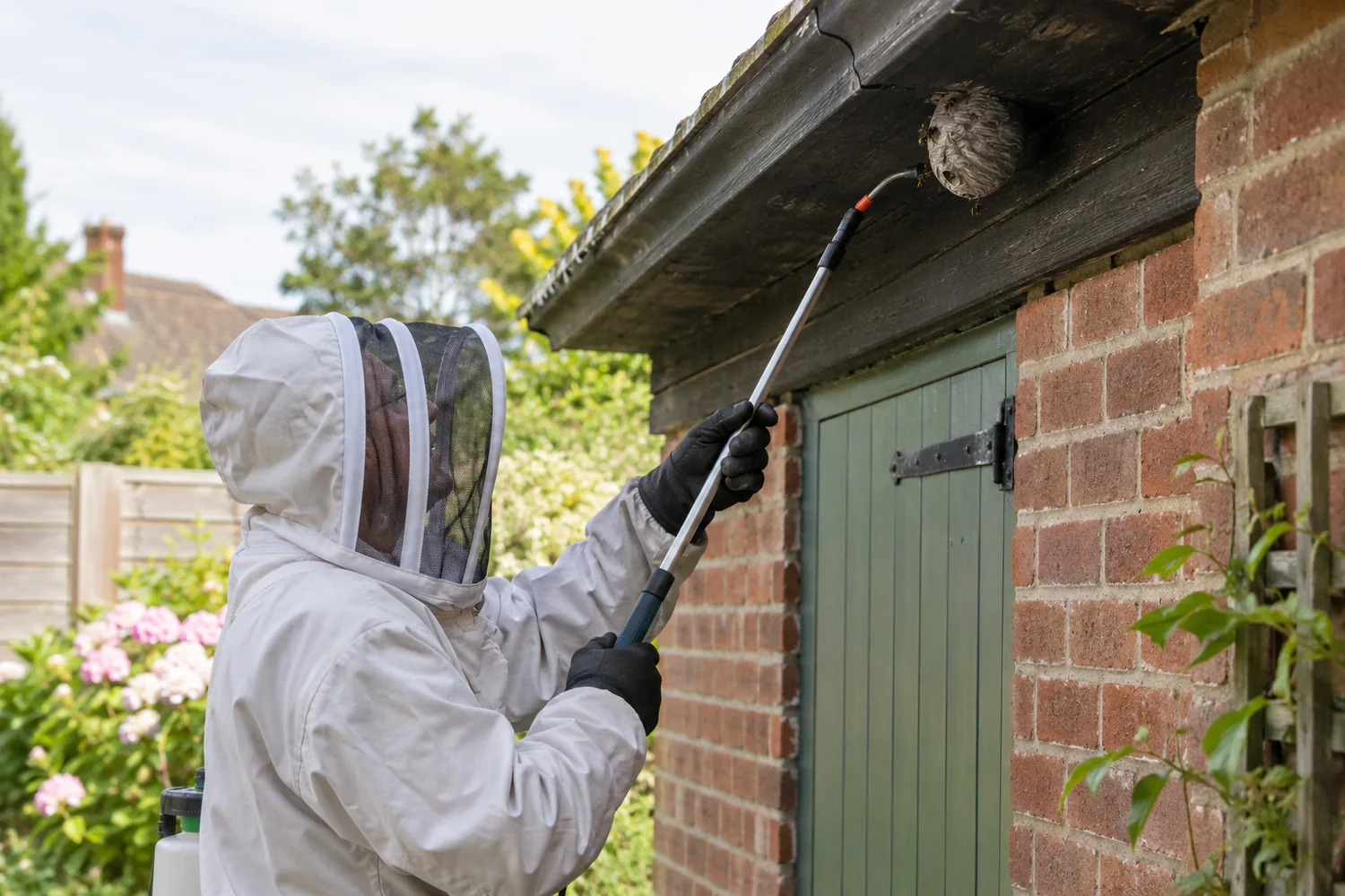 Protected technician inspecting a visible wasp nest beneath roof eaves